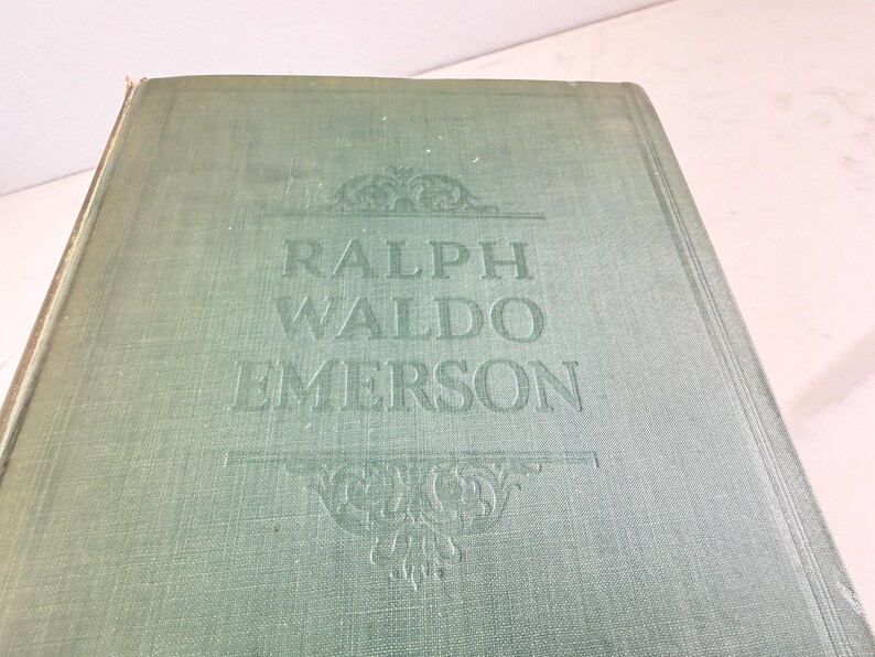 Puede incluir: Un libro antiguo con una cubierta verde descolorida. El t&iacute;tulo "RALPH WALDO EMERSON" est&aacute; grabado en letras may&uacute;sculas grandes. Adornos decorativos se encuentran arriba y abajo del t&iacute;tulo, agregando un toque cl&aacute;sico.