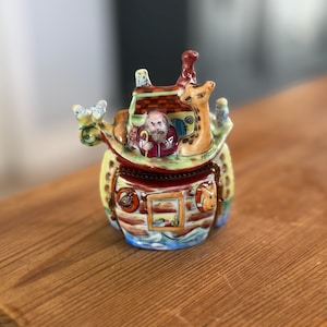 Op de afbeelding: Een witte keramische mok met een zwart handvat en de tekst "But First, Coffee" in een vetgedrukte, zwarte letter. De mok staat op een houten oppervlak. De mok is ongeveer 10 cm hoog.