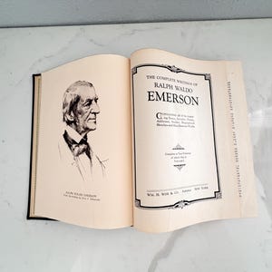Puede incluir: Libro abierto con el t&iacute;tulo "The Complete Writings of Ralph Waldo Emerson". El libro muestra un retrato de Emerson y los datos del editor. Las p&aacute;ginas son de color crema.