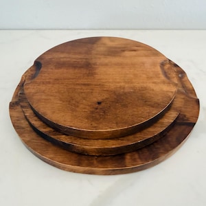 Puede incluir: Tres bandejas redondas de madera apiladas. Las bandejas son de madera marrón oscuro con vetas visibles y un acabado liso. Cada bandeja tiene un diámetro ligeramente diferente. La madera tiene un tono cálido.