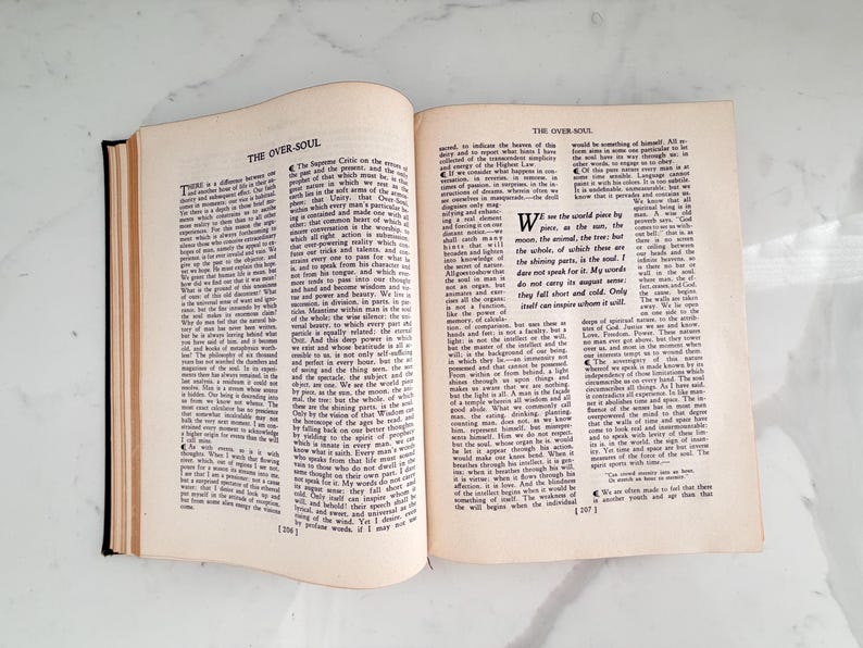 Puede incluir: Un libro abierto con el t&iacute;tulo "THE OVER-SOUL" en la parte superior de la p&aacute;gina. Las p&aacute;ginas est&aacute;n llenas de texto negro. El libro est&aacute; abierto sobre una superficie blanca.