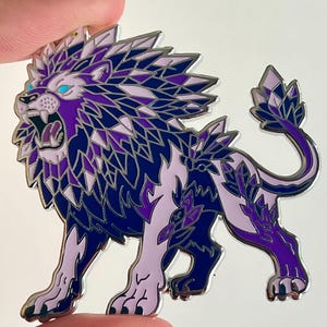 May include: A metal enamel pin shaped like a roaring lion with a geometric, crystalline mane and tail. The design features a color palette of deep navy blue, vibrant purple, and pale lavender, with bright cyan accents for the lion's glowing eyes.