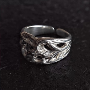 Puede incluir: Un anillo plateado con un diseño abierto y texturizado. El anillo presenta un patrón intrincado con múltiples aberturas. El diseño parece estar inspirado en formas orgánicas. El anillo se muestra sobre un fondo oscuro.