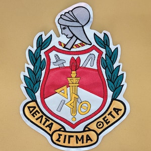 May include: Embroidered patch featuring the Delta Sigma Theta sorority crest. The crest includes a red shield with a torch, sword, and other symbols, surrounded by a laurel wreath. The patch has a white border and the Greek letters are in gold.
