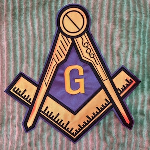 Könnte beinhalten: Ein Freimaurer-Emblem-Aufnäher mit einem Zirkel- und Winkeldesign in Gold und Schwarz, mit einem lila Zentrum. Der goldene Buchstabe "G" ist prominent dargestellt. Der Aufnäher ist wahrscheinlich für Kleidung oder Accessoires.