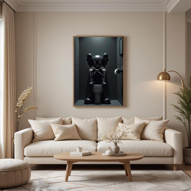May include: A framed artwork depicts a black cartoon figure seated on a toilet in a dark bathroom setting. The figure has large, round ears and crossed-out eyes. The artwork is displayed above a beige sofa with several pillows.