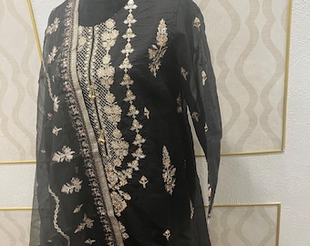May include: Black embroidered tunic with long sleeves, displayed on a mannequin. The tunic features intricate gold and cream-coloured floral embroidery along the neckline, sleeves, and front panel. The fabric appears to be sheer, with a delicate texture.