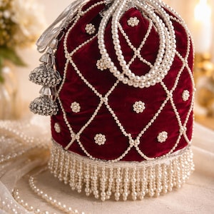 May include: A burgundy velvet pouch with a pearl beaded design. The pouch is adorned with pearl accents, a pearl fringe, and a silver drawstring. A pearl necklace is draped around the pouch.
