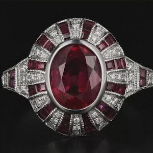 May include: A silver ring featuring a large oval ruby. The ruby is encircled by smaller rubies and diamonds in a sunburst pattern. The ring has a detailed, vintage design.