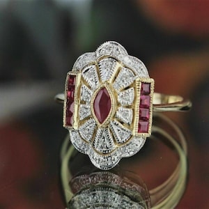 Peut inclure: Bague de style Art déco avec un anneau en or. La bague présente un rubis central de coupe marquise, entouré d'un halo de petits diamants et de rubis rectangulaires. Le sertissage est doré et argenté.