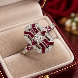 May include: A silver-toned ring featuring a central round brilliant-cut diamond surrounded by geometric patterns of deep red rubies and small pavé-set white diamonds. The intricate metalwork creates an open, layered design with a polished finish.