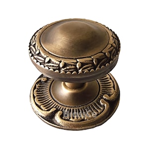 May include: An antique brass door knob with a round, domed top and a decorative floral border. The base features an ornate, stylized design. This hardware piece is ideal for adding a vintage touch to doors and cabinets.