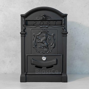 May include: Black cast iron post box with the word "POST" across the top. It features a lion crest and a lower compartment with a keyhole. The brand name "BrassCo" is visible at the bottom.