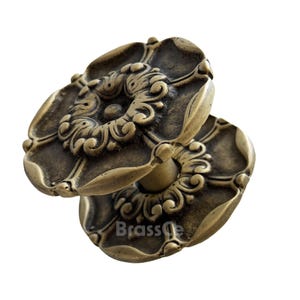 Può includere: Due pomelli per porte antichi in ottone con un design floreale ornato. I pomelli hanno un aspetto invecchiato e usurato, con dettagli intricati e una calda tonalità dorata. La parola "BrassGe" è stampata nella parte inferiore dell'immagine.