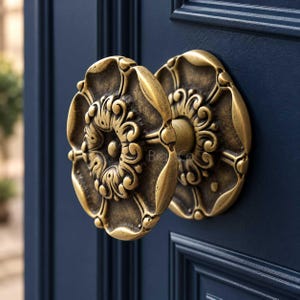 May include: A round, antique brass door knob featuring an intricate, raised floral relief pattern with a central circular detail. The knob is mounted on a dark navy blue door with recessed paneling, showcasing a weathered, metallic finish.