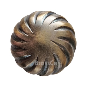 Puede incluir: Un pomo de armario de color bronce con un diseño en espiral. El pomo redondo tiene una superficie texturizada. El texto "BrassCe" es visible en la parte inferior derecha del pomo.