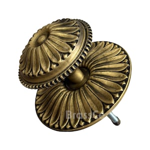 Pode incluir: Dois puxadores de armário de latão antigo com um design floral. Os puxadores têm formato redondo com um padrão detalhado de pétalas e uma borda texturizada. Os puxadores são montados em um parafuso de metal.