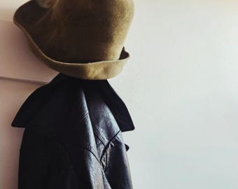 以下が含まれることがあります： 幅の広い襟と質感のある表面を持つダークブラウンのレザージャケットと、丸みを帯びたクラウンとわずかに反り返ったつばが特徴のタンカラーのフェルトハット。両方のアイテムが一緒に配置されており、それぞれの独特な質感と色合いが表現されています。