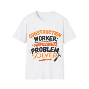 May include: A white short-sleeve t-shirt featuring the orange and black text CONSTRUCTION WORKER: PROFESSIONAL PROBLEM SOLVER. The graphic includes a small illustration of a nail and a hammer positioned near the bottom right of the text.