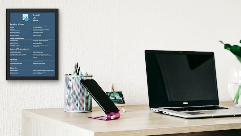 Pu&ograve; includere: Un'area di lavoro con un laptop, uno smartphone e un poster incorniciato "Docker CLI Sheet". Lo smartphone &egrave; appoggiato su un supporto viola. Un vaso trasparente con foglie verdi &egrave; sulla destra. La scrivania &egrave; in legno chiaro.