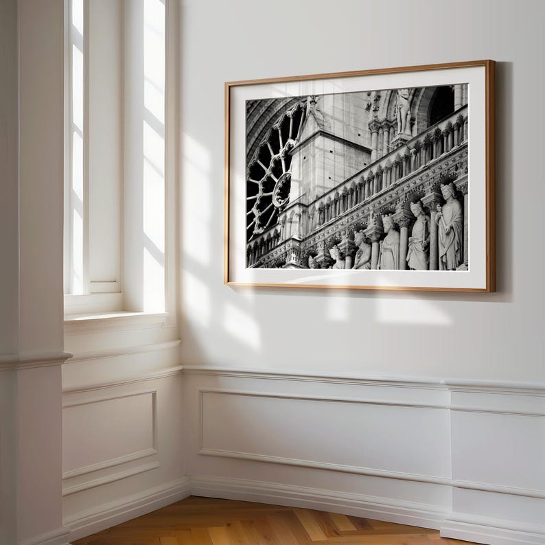 May include: A black and white framed wall art print depicting the architectural details of the Notre-Dame Cathedral in Paris, featuring a prominent rose window and a row of stone statues of figures standing along the gallery of the facade.