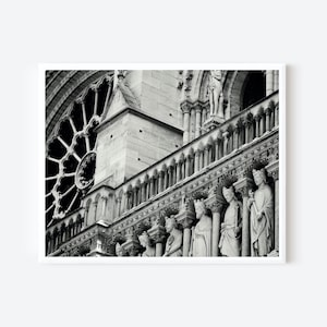 May include: A black and white architectural photograph of the Notre-Dame Cathedral facade, featuring a large circular rose window, stone columns, and a row of carved stone statues of figures standing in niches along the gallery of kings.