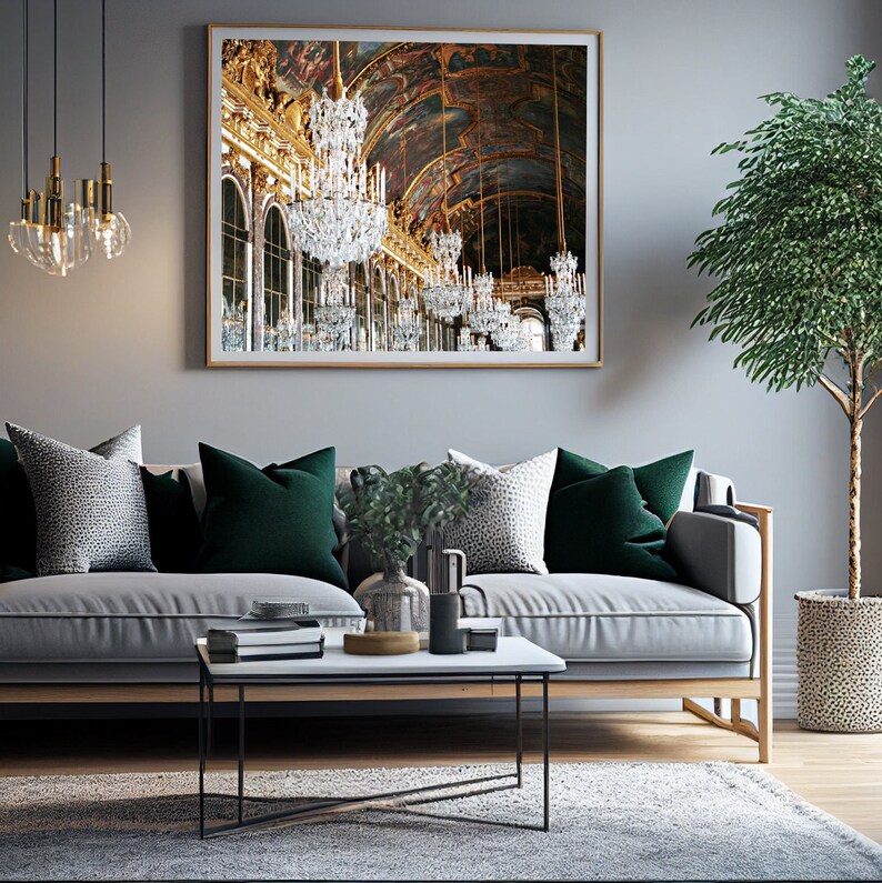 Puede incluir: Un sof&aacute; gris con almohadas de terciopelo verde y una almohada con estampado blanco y negro. Una mesa de centro con tapa blanca y patas de metal negro se encuentra frente al sof&aacute;. Una planta en maceta y una impresi&oacute;n enmarcada de un gran sal&oacute;n con l&aacute;mparas de ara&ntilde;a cuelgan en la pared detr&aacute;s del sof&aacute;.
