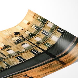 May include: A curved photographic print depicting a Parisian-style building with beige stone walls, multiple windows, and dark metal balconies. A tall black street lamp stands in the foreground, while the lower portion shows a blurred wooden texture.