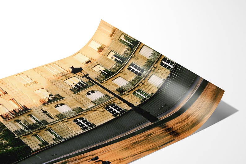 May include: A curved photographic print depicting a Parisian-style building with beige stone walls, multiple windows, and dark metal balconies. A tall black street lamp stands in the foreground, while the lower portion shows a blurred wooden texture.