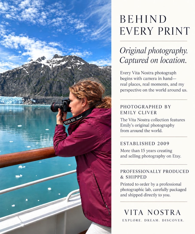 May include: A person in a maroon jacket uses a black DSLR camera to photograph a glacier and blue water from a ship deck. Text on the right reads: BEHIND EVERY PRINT, Original photography. Captured on location, PHOTOGRAPHED BY EMILY CLIVER, ESTABLISHED 2009, PROFESSIONALLY PRODUCED & SHIPPED, VITA NOSTRA EXPLORE. DREAM. DISCOVER.