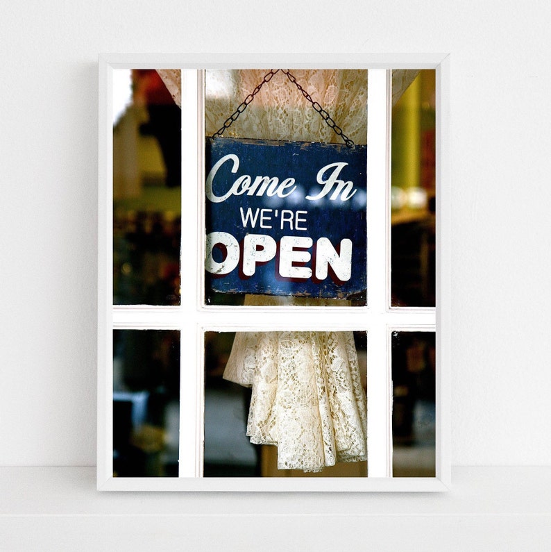 Open sign navy blue and white photography print from the Magnolia Bakery in New York City.   Warm welcoming image with a vintage lace curtain and charming Come In We're Open wood sign.   Unique non-traditional open sign available for sale framed.