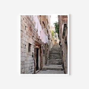 May include: A narrow, stone alleyway in a European city with white laundry hanging on a clothesline. The alleyway leads up a set of stone steps.