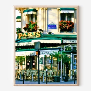 Vibrant colorful photography print of Paris Saint Germain cafe in the heart of Paris France.  Green awnings, a neon yellow sign and pops of red and pink from the flower boxes in the windows above  bistro tables and chairs lining sidewalk.