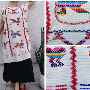 May include: A white embroidered dress with colorful bird designs. The dress features short sleeves and a long, flowing skirt. The embroidery includes red, blue, yellow, and green thread, creating a vibrant pattern. The dress is a unique piece of clothing.