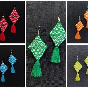 May include: A collection of handmade diamond-shaped earrings in various colors. Each pair features a geometric embroidered design and a matching tassel. Colors include red, green, orange, blue, and yellow, with white embroidery.