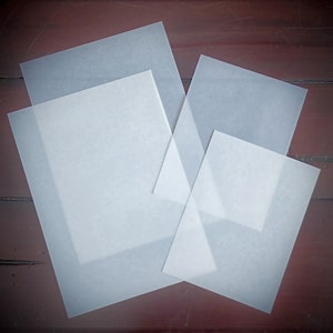May include: Four sheets of white translucent paper, stacked on top of each other, on a dark brown wooden surface.