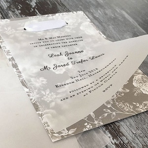 Może przedstawiać: Białe zaproszenie ślubne z kwiatowym wzorem i białą wstążką. Zaproszenie brzmi: "Mr. & Mrs. Mastero zapraszają do wsp&oacute;lnego świętowania ślubu ich c&oacute;rki Leah Joanne z Mr. Jaredem Treforem Lewisem. 14:00, 2 lipca 2018, Kingdom Hall, Havertown, po kt&oacute;rym nastąpi przyjęcie i wiecz&oacute;r z muzyką i tańcem w Zamku Picton RSVP"