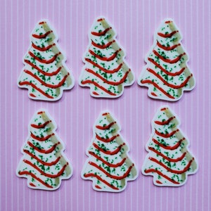 May include: Six white Christmas tree-shaped cookies with red and green icing. The cookies are decorated with red and green sprinkles.