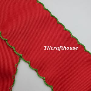 May include: Close-up of a red ribbon with a ribbed texture and a green, scalloped edge. The text "TNcrafthouse" is visible in white on the ribbon. The ribbon is likely used for crafting or gift wrapping.
