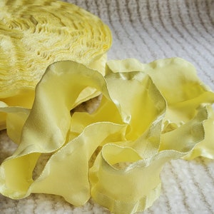May include: A roll of yellow ruffled ribbon with a satin finish. The ribbon is folded and stacked, showing the ruffled edges.