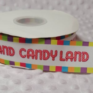 May include: White ribbon with multi-colored stripes and the text "Candy Land Candy" in pink.