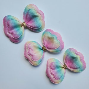 May include: Three pastel rainbow-colored layered felt hair bows with gold glitter centers.