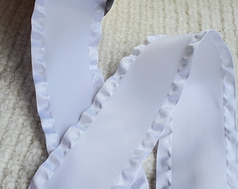 May include: White satin ribbon with a scalloped edge. The ribbon is folded in half and the edges are visible.