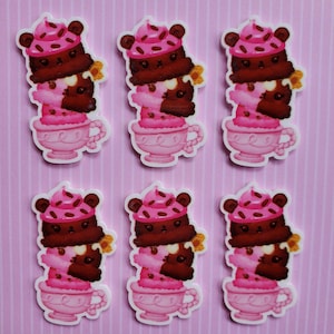 May include: Six pink and brown cartoon bear ice cream sundaes in a teacup. Each sundae has a chocolate ice cream layer, a pink ice cream layer, and a brown bear wearing a pink hat with sprinkles on top.