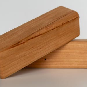 Puede incluir: Dos borradores rectangulares de madera con un acabado marrón claro. Un borrador descansa sobre el otro. La parte inferior de cada borrador tiene una almohadilla de fieltro negro para borrar. La veta de la madera es visible.