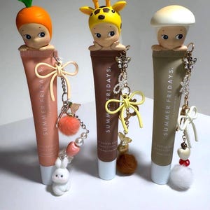 以下が含まれることがあります： Summer Fridays Butter Balmのリップバームチューブ3本。それぞれユニークなフィギュアとチャームで飾られています。1つはニンジンをかぶったフィギュア、もう1つはキリン、最後はキノコです。各チューブには、ウサギ、蝶、リボンなど、異なるチャームが付いています。