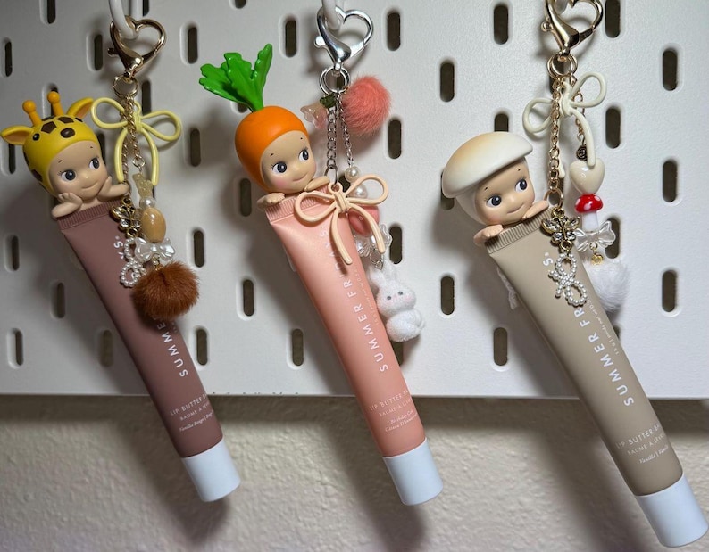 以下が含まれることがあります： リップバターのチューブから出てくる小さなフィギュアが特徴の、3つの装飾的なキーホルダー。フィギュアはキリン、ニンジン、キノコです。各キーホルダーは異なる色のチューブで、チャームと金属製の留め金で飾られています。