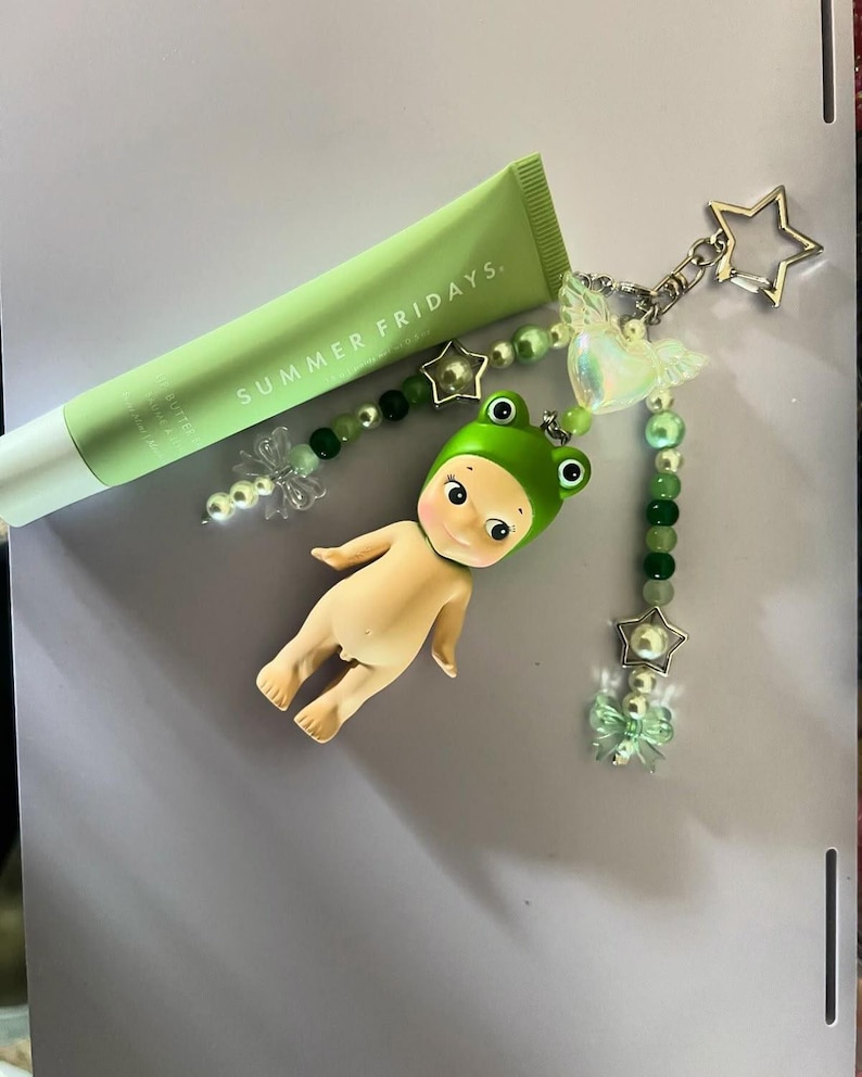 以下が含まれることがあります： サマーフライデーズのライトグリーンのチューブ製品と、カエルの帽子をかぶった小さな人形、グリーンのビーズ、星型のチャームが付いたチャーム。チャームには、透明な蝶と星型のキーホルダーも含まれています。