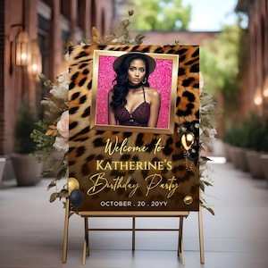 May include: A gold-framed sign with a leopard print background and a photo of a person in a hat. The sign reads "Welcome to Katherine's Birthday Party" in gold script, with the date "OCTOBER . 20 . 20YY" below. Decorative balloons and floral arrangements are also present.