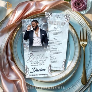 May include: A formal table setting with light blue plates, gold silverware, and a menu card. The menu card features a photo of a man and text that reads "Welcome to Birthday Dinner in the Honour of Darius 25th Birthday Celebration."
